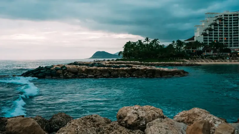 A stunning ocean view at Ko Olina, Hawaii with a resort and rocky shore under dramatic skies.