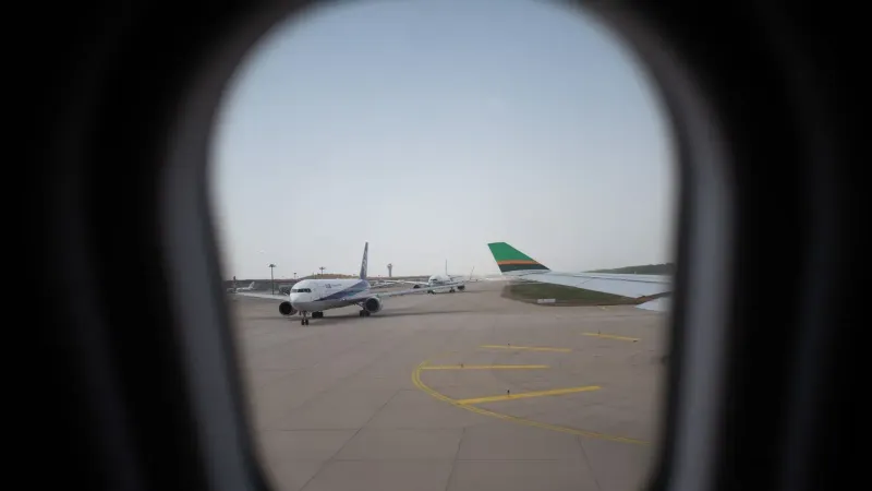 Avión visto a través de una ventana, estacionado en la pista del aeropuerto, capturando un momento de viaje.