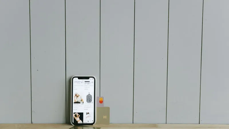 A smartphone displaying an ecommerce site with a credit card, set on a wooden surface, depicting online shopping.