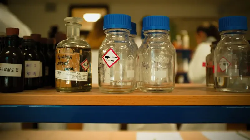 Vista de cerca de botellas de vidrio y contenedores en un estante de laboratorio con símbolos químicos.