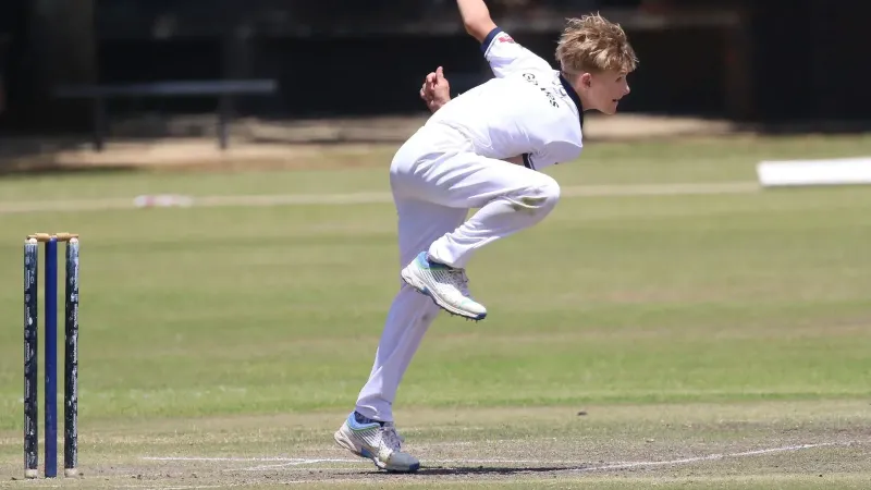 Joven jugador de críquet en acción en un día soleado, capturado en medio de los bowls con un enfoque intenso.