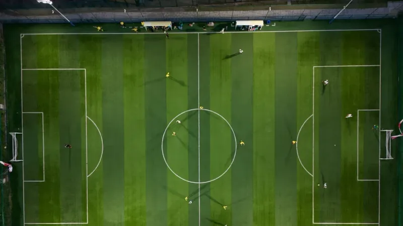 Dynamic aerial shot capturing a soccer match on a vibrant green field at night.