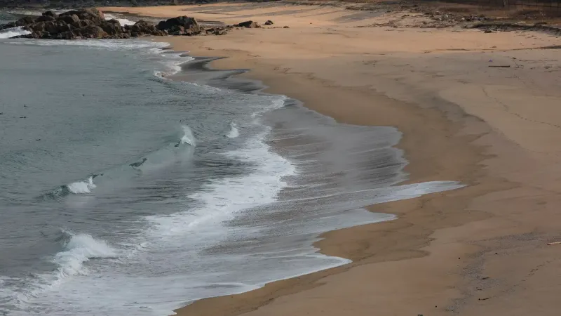 Playa de arena tranquila con suaves olas, ideal para relajación y tranquilidad.