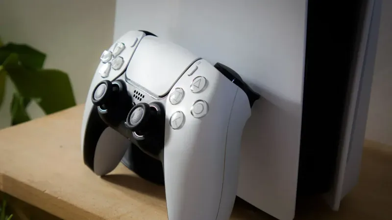 Close-up of PlayStation 5 with DualSense controller on a wooden shelf.