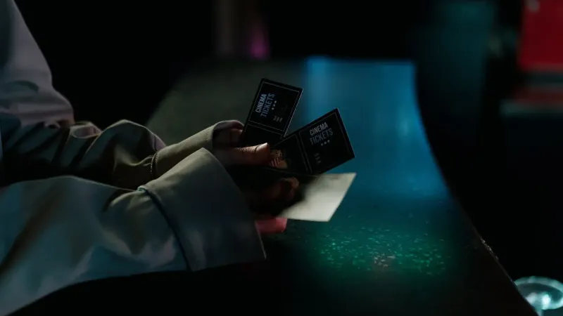 Imagen de mal humor de una persona con entradas de cine por la noche, destacando la anticipación de una noche de cine.