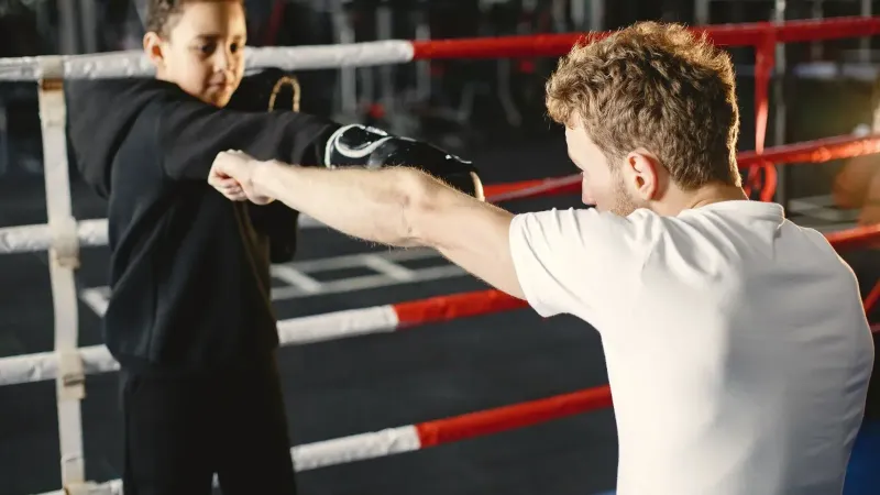 Un joven practica técnicas de boxeo con un entrenador en un gimnasio. Tutoría en deportes.