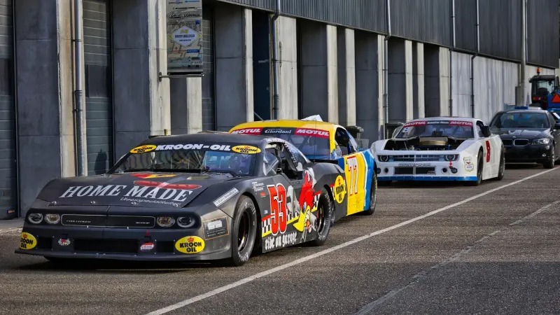 Una hilera de coloridos carros alineados en un garaje de carreras, listo para la acción del automovilismo.