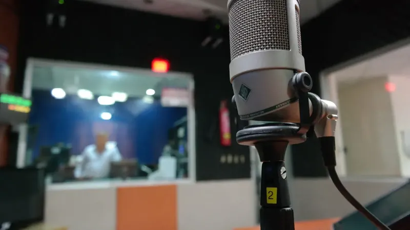 Primer plano de un micrófono en un estudio de grabación con un ingeniero de sonido borroso en el fondo.