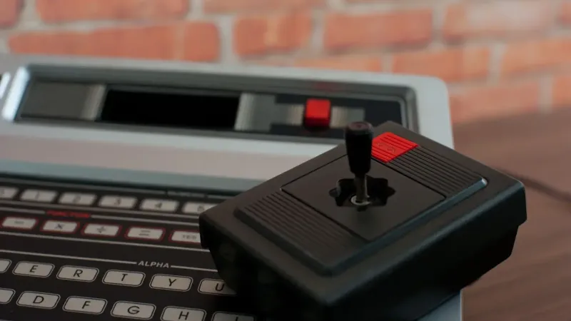 Un primer plano de una consola de juegos Philips Odyssey 2 vintage y joystick contra una pared de ladrillo.