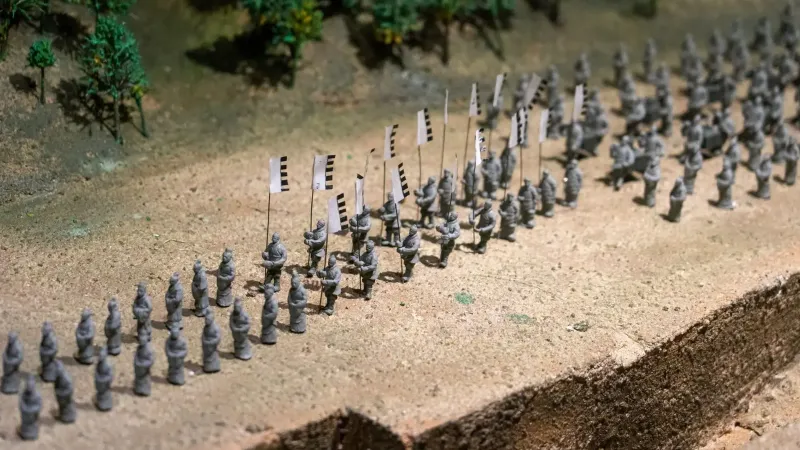 Close-up of a miniature army model with flags, depicted in a diorama scene.