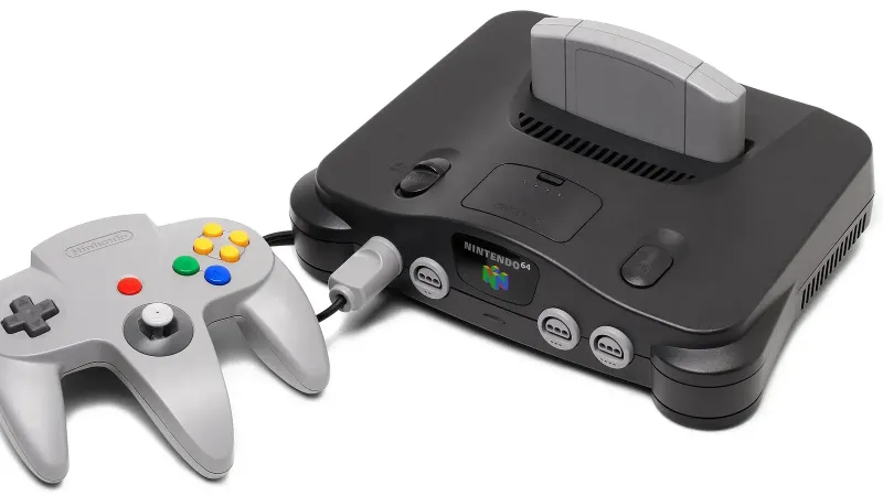 Se muestra una consola de videojuegos Nintendo 64 con un controlador gris.