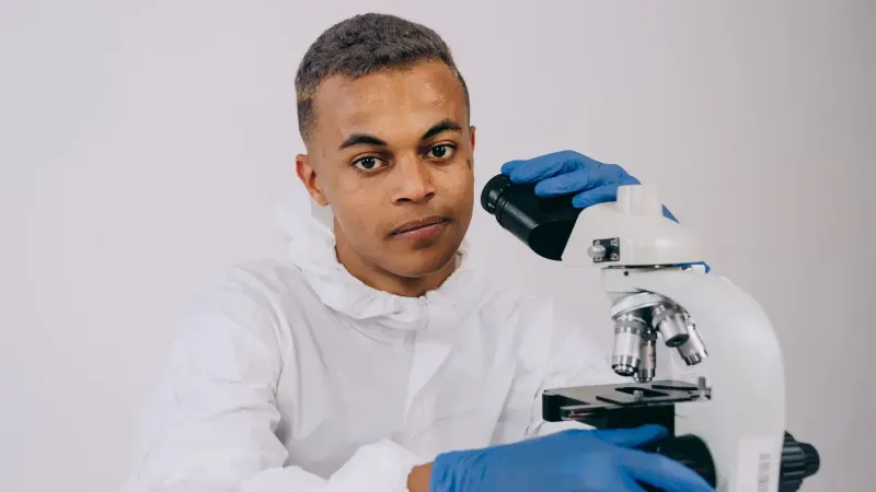 Científico en equipo de protección examinando muestras a través de un microscopio en un laboratorio.