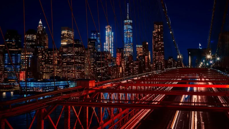 A breathtaking night view featuring the New York City skyline and iconic Brooklyn Bridge illuminated in vibrant colors.