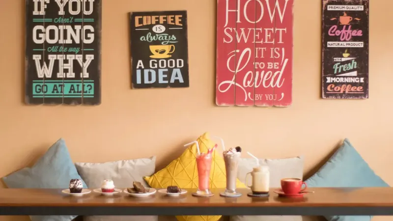 Acogedor interior de café con bebidas y postres sobre una mesa de madera, rodeado de decoración artística de la pared.