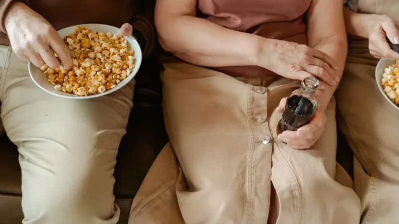 Tres personas disfrutando de palomitas y refrescos en un sofá. Ambiente relajado e informal.