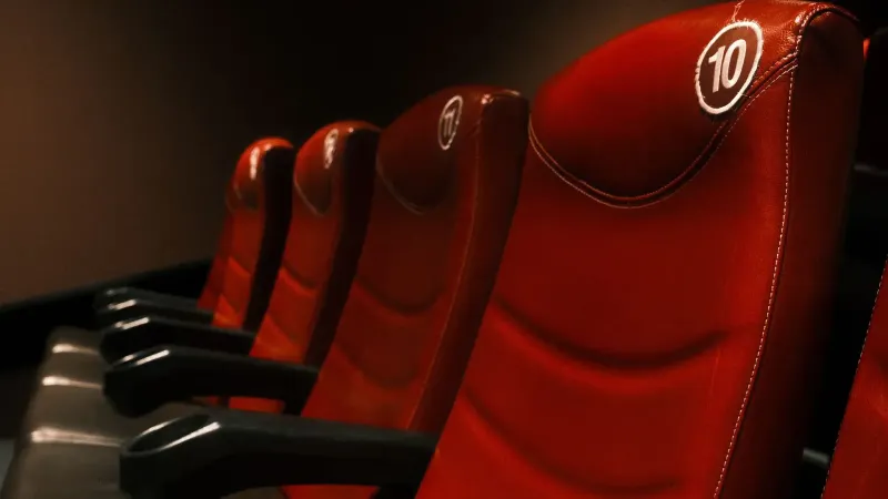 Fila de lujosos asientos de cine rojo con reposabrazos en un teatro con poca luz.