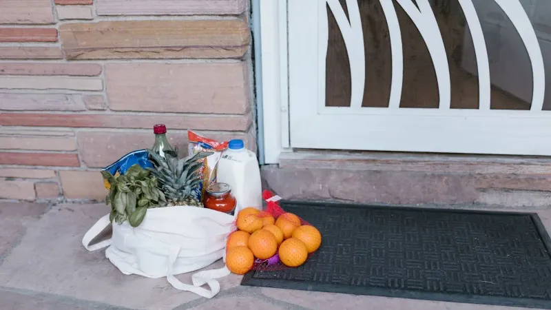 Reusable bag with groceries and fruits left at doorstep, highlighting delivery service.