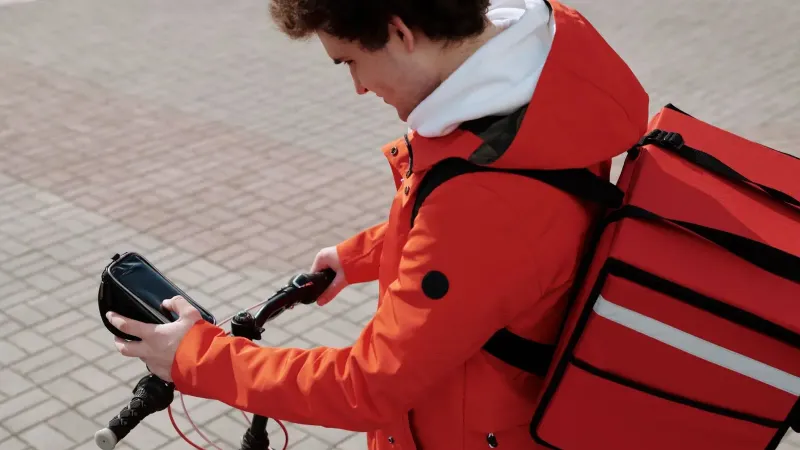 Ciclista de entrega de alimentos comprobando el teléfono inteligente mientras se trabaja. Estilo de vida urbano y tecnología.