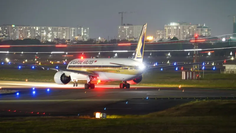 Un avión de Singapore Airlines en la pista por la noche en medio de las luces de la ciudad y las luces del aeropuerto.