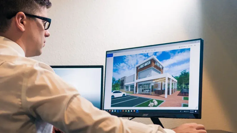 Architect evaluating a building design on a computer screen in an office setting.