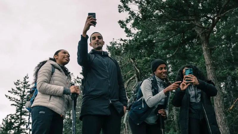 Cuatro amigos disfrutando de una caminata, capturando el momento con selfies en un entorno escénico al aire libre.