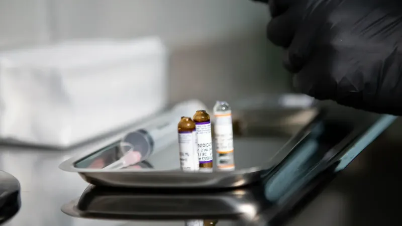 Primer plano de viales médicos y jeringa en bandeja de acero inoxidable en entorno clínico.