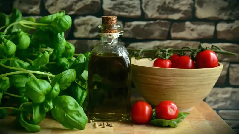 Imagen que muestra albahaca, tomates y un frasco de aceite de oliva.