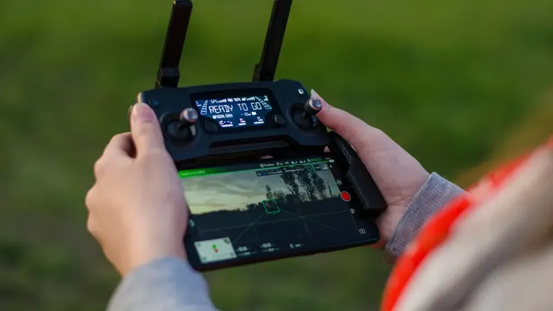 Close-up of hands holding a DJI drone controller outdoors with green background.