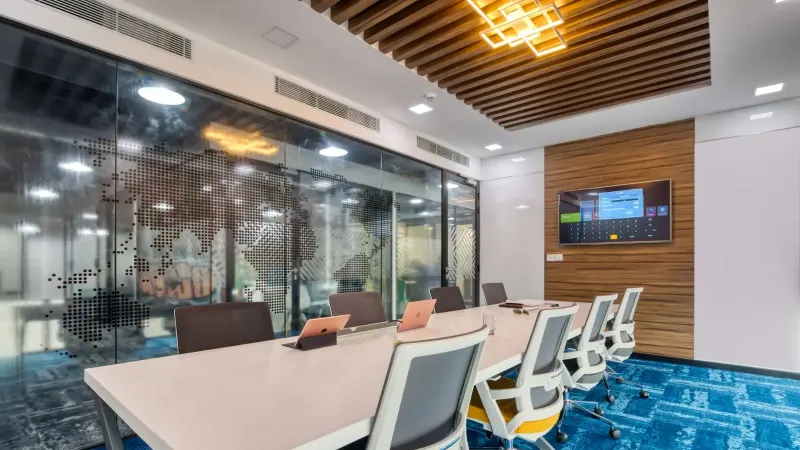 Sala de juntas elegante y contemporánea con paredes de vidrio, muebles modernos y pantalla digital.