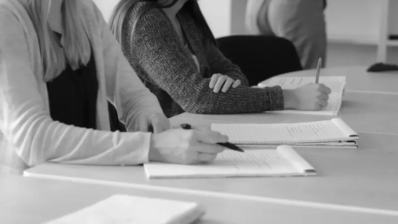 Imagen en blanco y negro de estudiantes escribiendo notas durante una reunión.