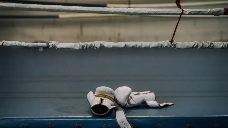 White boxing gloves resting inside an empty boxing ring, symbolizing sports intensity.