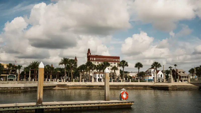 Vista panorámica de la costa de San Agustín con edificios históricos y palmeras bajo un cielo nublado.