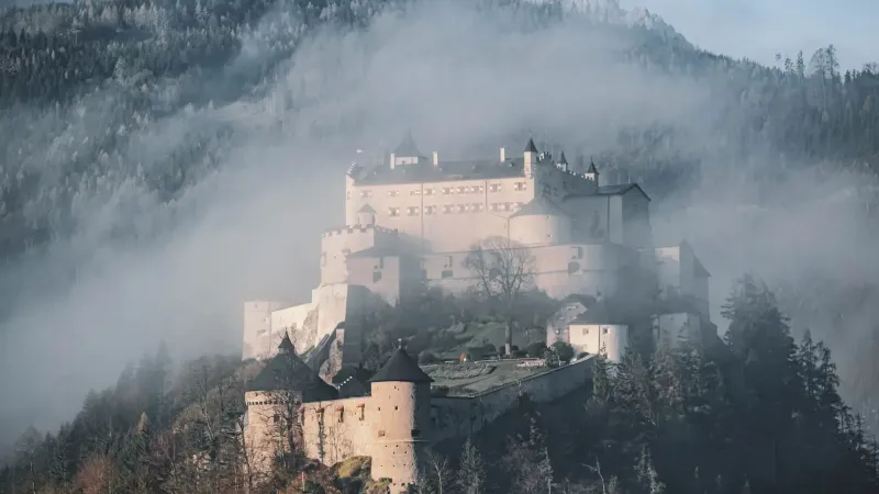 Una vista impresionante del castillo de Hohenwerfen envuelto en niebla, rodeado de bosques alpinos.