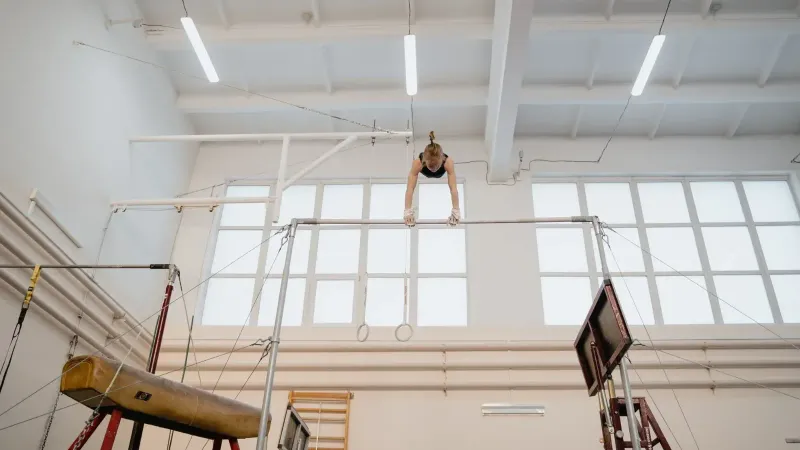 Gimnasta femenina joven practicando hábilmente en barras desiguales en un entorno de gimnasio brillante.