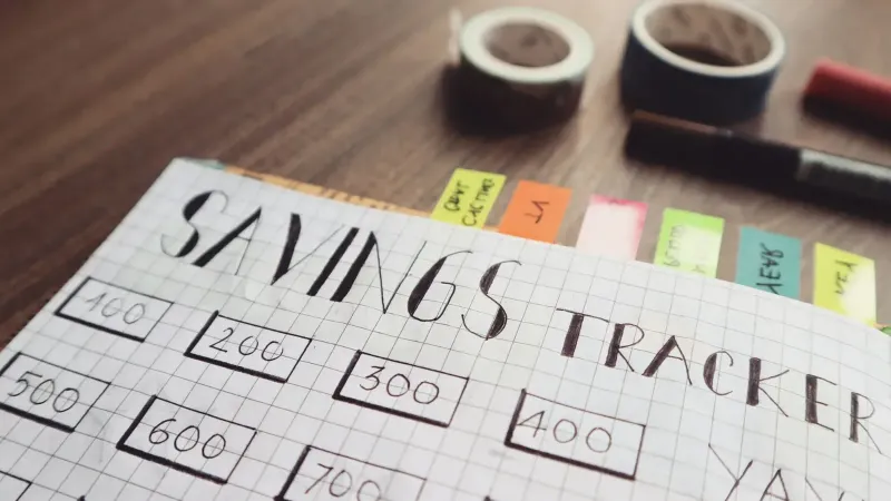 Primer plano de un rastreador de ahorros hecho a mano con pestañas de colores sobre una mesa de madera, ideal para la planificación financiera.