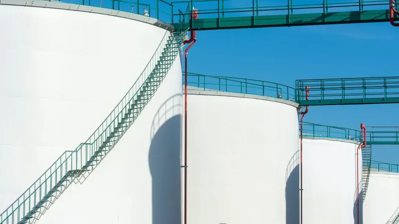 Grandes tanques de almacenamiento industrial con una pasarela verde bajo un cielo azul claro.