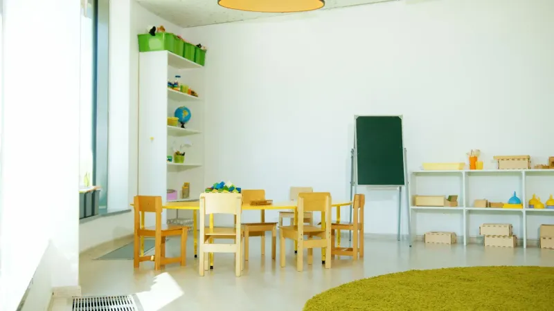 Un salón de clases de jardín de infantes colorido y bien iluminado con sillas, mesas y materiales educativos.
