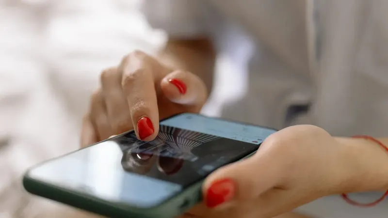 A person with red nails using a smartphone with a touch screen interface.