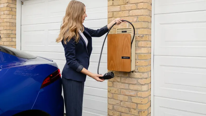 A woman using a home electric vehicle charger on a brick wall in a garage.