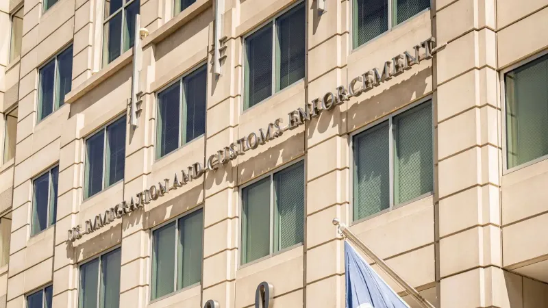 Vista exterior del edificio de Inmigración y Control de Aduanas de EE. UU. con una bandera y señalización visibles.