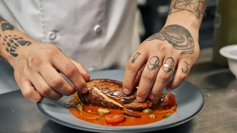 Un chef con tatuajes coloca hábilmente un plato gourmet en una cocina profesional.