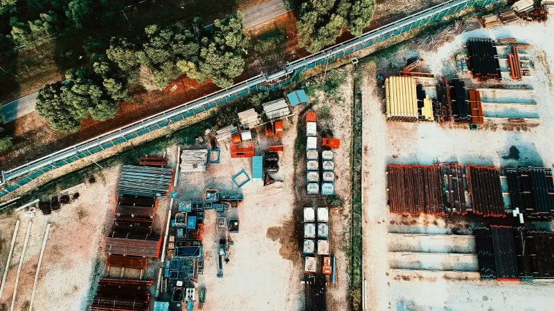 Una toma aérea detallada que muestra una instalación de almacenamiento industrial al aire libre con materiales metálicos y rodeado de árboles.