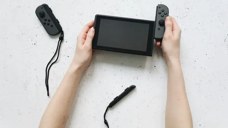Primer plano de las manos ensamblando una consola Nintendo Switch con controladores separados en una superficie blanca.