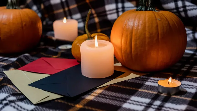 Cálida escena de Halloween con calabazas, velas y sobres sobre fondo a cuadros.