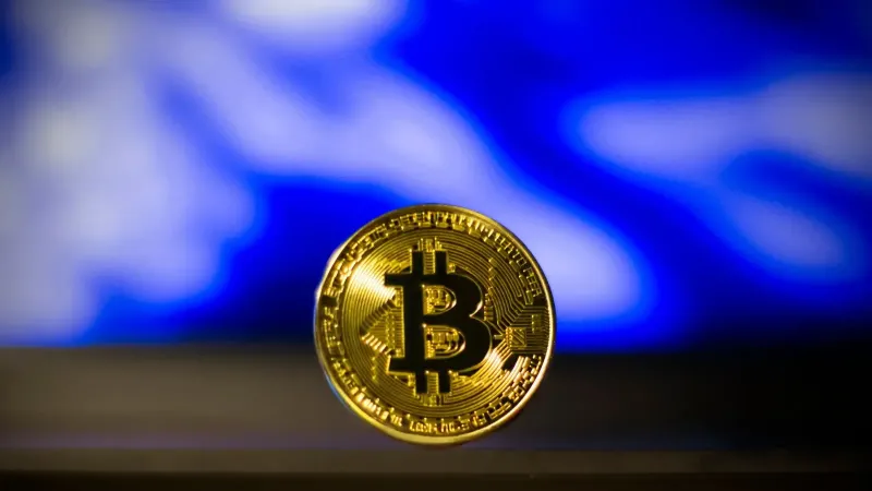 Close-up de una moneda de bitcoin de oro con un fondo abstracto azul borroso, simboliza la moneda digital.