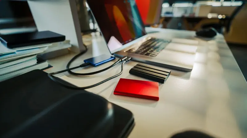 Un escritorio de oficina cuidadosamente organizado con una computadora portátil y varios discos duros externos, perfecto para un espacio de trabajo digital.