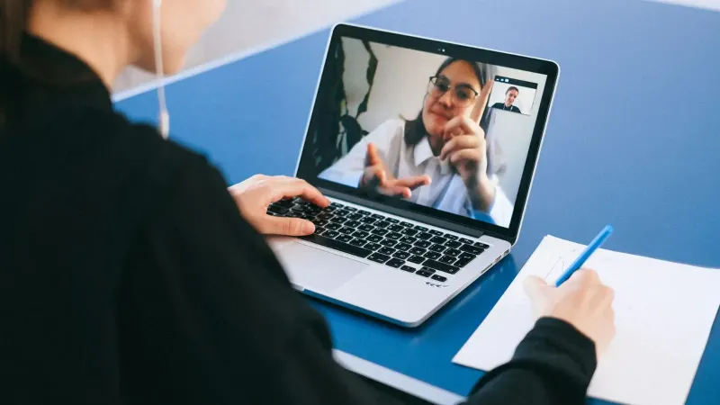 Mujer participando en una reunión virtual, tomando notas durante una videoconferencia en una computadora portátil.