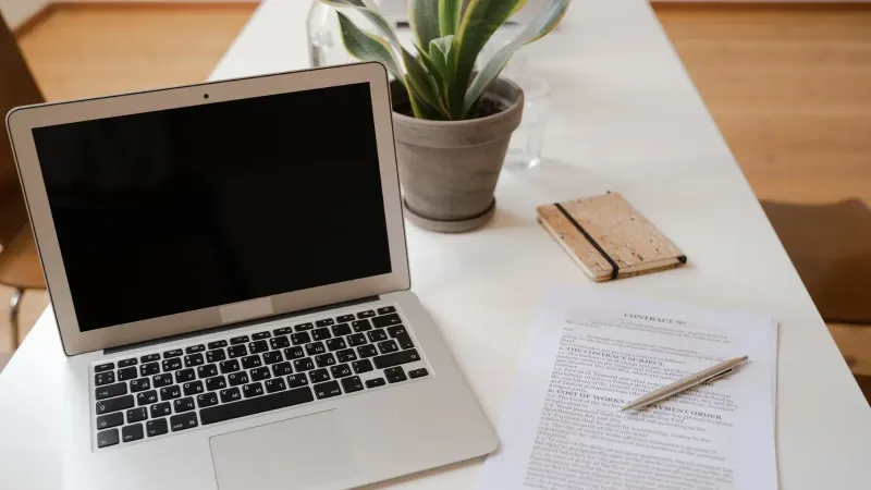 Una configuración de escritorio de oficina serena con un documento de computadora portátil, de planta y de contrato ideal para temas de negocios.
