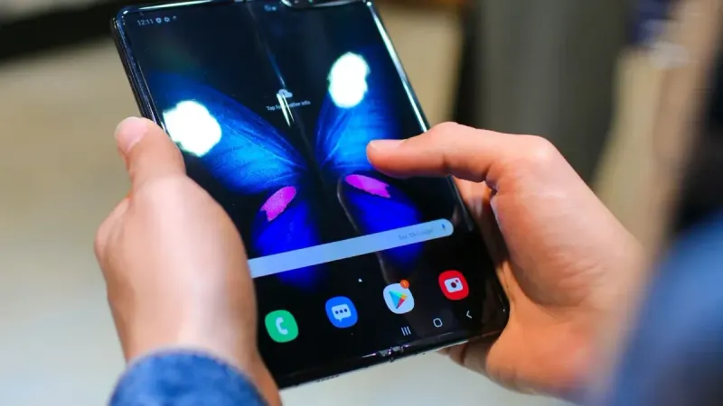 Close-up de manos sosteniendo un smartphone plegable que muestra una mariposa en la pantalla.