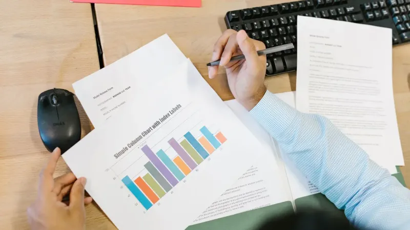 Un analista de negocios revisa un colorido gráfico de barras y documentos en un escritorio, lo que indica el análisis de datos.